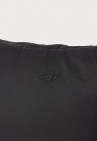 Cojín negro hecho de tela suave, con un logo en relieve. Forma rectangular simple con textura lisa y sin patrones visibles.
