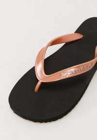 Sandále Calvin Klein s čiernou gumovou podrážkou a kovovými strapcami v ružovom zlate. Strapy sú elegantné s embosovanou značkou.