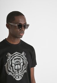 Camiseta negra con un gráfico de tigre blanco; gafas de sol con marco transparente y lentes oscuros, textura suave y diseño rectangular.