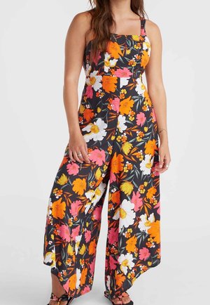 Kvinde iført sort ærmeløs jumpsuit med vide ben og lyst orange, hvidt, pink og gult blomsterprint.