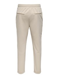Beige jogger pants with a soft texture, elastic waistband, two back pockets with zippers, tapered leg, and cuffed hem.