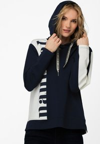 Mørkeblå og hvid hætte sweatshirt med et stort print på den ene side, der har snore med brandtekst og et blødt, struktureret stof.