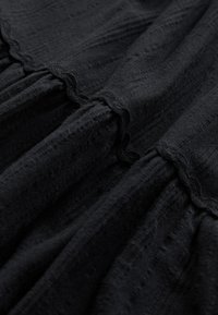 Czarna tkanina o teksturowanym wykończeniu, z marszczonymi sekcjami i falistym brzegiem. Gładki, lekki materiał z subtelnym wzorem.