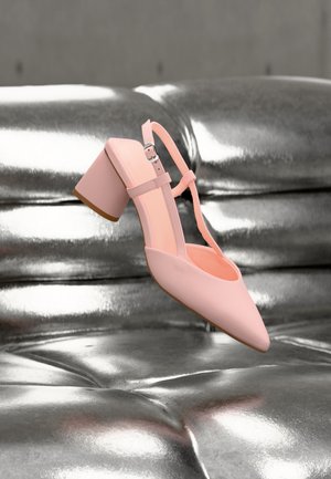 Rosa Blockabsatzschuh mit Knöchelriemen, der über einer glänzenden silbernen gesteppte Lederoberfläche schwebt.