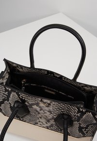 Handväska med mönster av svart och grå ormskinn och svarta läderhandtag. Rymligt inre med en ficka med dragkedja och detaljer i guld.