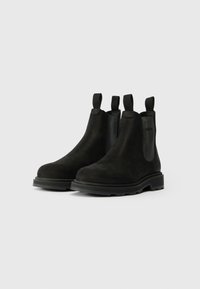 Bottines Chelsea en daim noir avec panneaux élastiques sur les côtés et languettes de tirage. Bout arrondi et semelle en caoutchouc avec des détails de traction.
