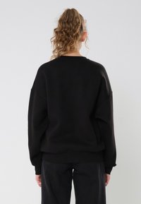 Black oversized sweatshirt with a crew neckline, drop shoulders, and ribbed cuffs. Smooth texture, minimal detailing, and relaxed fit.