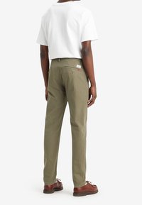 Olivgrön byxor med rak benform, tillverkade av bomull. Har två bakfickor, en etikett och är matchade med bruna skor.