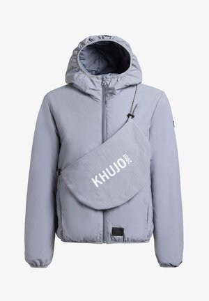 Světlé šedé kapucí opatřené sako s předním zipem a šikmou kabelkou v odpovídající barvě s nápisem "KHUJO 2001" přes hruď.