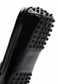 Chaussure en cuir noir avec une finition lisse, forme semi-arrondie et picots en caoutchouc texturé sur la semelle pour plus d'adhérence.