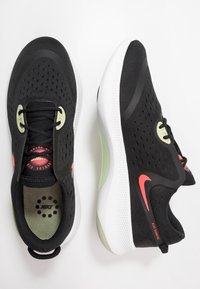 Zapatillas de running negras de Nike con malla perforada, con media suela blanca, detalles en verde y logo rojo; presentan un diseño con cordones y una pestaña en el talón.