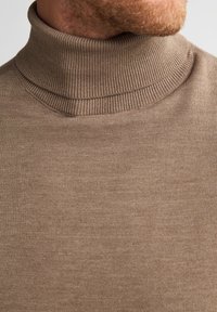 Pull à col roulé marron en tricot doux et lisse. Doté d'un col et d'un ourlet côtelés avec une coupe ajustée.