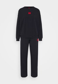 Zwarte sweatshirt en bijpassende broek van zachte stof. Bevat een rood logo-detail op de borst en een klein vergelijkbaar label op de broek.