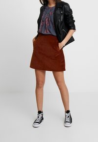 Brown corduroy mini skirt with pockets, paired with a floral-patterned gray blouse and black leather jacket. Worn with black high-top sneakers.