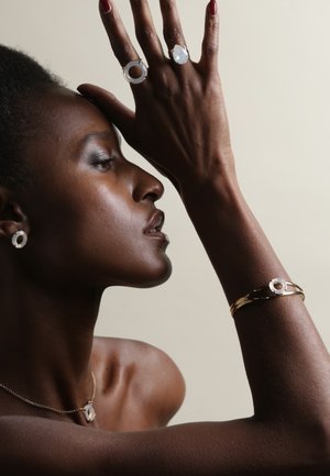 Gouden en zilveren sieraden met cirkelvormige ontwerpen; gelaagde ringen met een doorschijnende steen, bijpassende oorbellen en een delicate ketting.