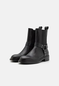 Black leather ankle boots with a smooth finish, elastic side panels, a decorative strap with metal accents, and a low block heel.