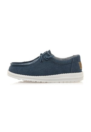 Zapatilla azul de tela tipo slip-on con un acabado texturizado, suela de goma blanca y costuras de acento. Presenta un detalle decorativo de cordones en la parte frontal.