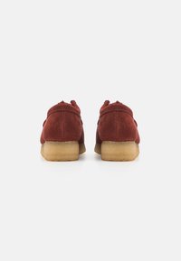 Chaussures en daim marron avec un bout arrondi et un petit talon, présentant une texture lisse et un design minimaliste. Vue arrière montrant l'absence de lacets.