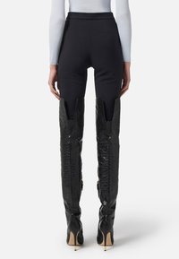Pantaloni alti neri dalla linea elegante, abbinati a stivali alti fino al ginocchio in pelle stampata coccodrillo, con punte affusolate e tacchi a spillo.