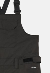 Sorte vanntette bib-overaller med justerbar stropp, lokk til frontlommen, side-Velcro-stropp, og "DRYVENT"-merke nederst til høyre.