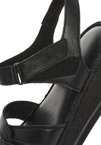 Sandale en cuir noir avec bride réglable et semelle intérieure rembourrée, avec une semelle plateforme texturée pour plus de hauteur et de confort.