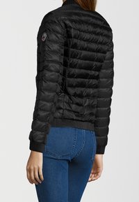 Svart puffjacka med quiltad design och ribbad mudd. Har en hög krage och logotypdetalj på vänster ärm. Bärs över denimjeans.