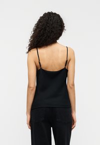 Μαύρη σατέν καμιζόλη με λεπτές ρυθμιζόμενες τιράντες, σχεδιασμένη με ίσια πλάτη και λεία υφή. Συνδυάζεται με σκούρα τζιν παντελόνια.