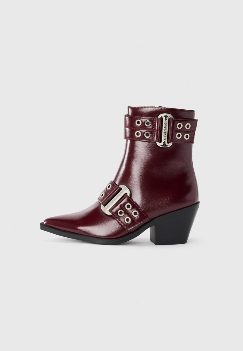 Burgunderfarbene Leder-Stiefelette mit spitz zulaufender Zehenpartie, doppelten Schnallenriemen, silbernen Akzenten und niedrigem Blockabsatz. Glatte, glänzende Oberfläche.