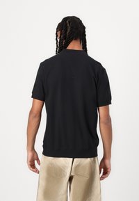 Czarna bluzka z krótkim rękawem, okrągłym dekoltem i ribbowanym dołem, wykonana z gładkiego materiału. Prosty design, bez widocznych wzorów ani akcentów.