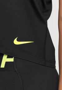 Top atletico nero in tessuto traspirante con il logo giallo del swoosh Nike. Ha una vestibilità rilassata e un design senza cuciture per il massimo comfort.