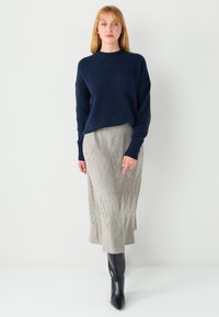 Marineblauer Strickpullover mit lockerem Schnitt, kombiniert mit einem hellgrauen, gerippten Midirock mit Zickzackmuster und schwarzen Overknee-Stiefeln.