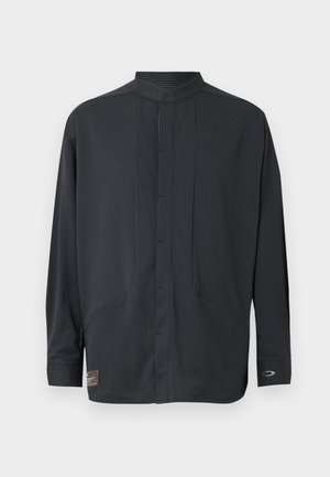 Long-sleeved black button-up shirt with a mandarin collar, featuring vertical pinstripes, two side pockets, and a branded patch at the hem.