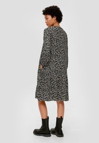 Blumenkleid mit langen Ärmeln in Schwarz und Weiß, mit lockerem Schnitt und Seitentaschen, kombiniert mit schwarzen Stiefeletten.