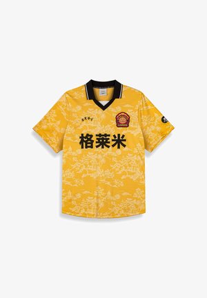 Gelbes Kurzarmtrikot mit schwarzem Kragen. Es hat ein weißes Blumenmuster und schwarzen Text. Enthält ein rotes Logo auf der linken Brust.