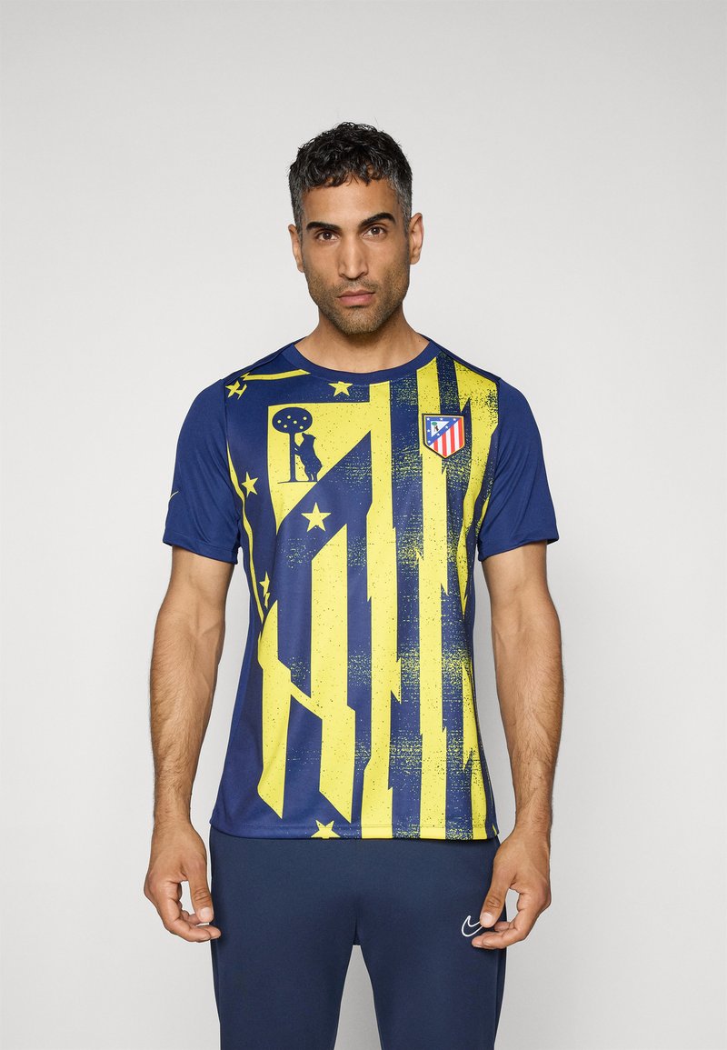 Blå sports t-shirt med gule grafiske striber og mønstre. Har et logo på brystet. Korte ærmer og rund hals.