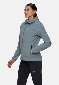 Giacca softshell grigia chiara con cappuccio, tasche con zip e polsini elastici. Caratterizzata da un logo discreto sulla manica e un design testurizzato.