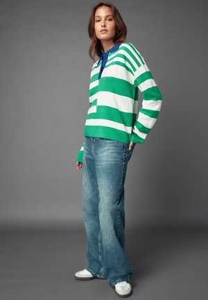 Grøn- og hvidstribet sweater med en blå krave, parret med lyseblå flagrende jeans og hvide sneakers. Glat tekstur, afslappet design.