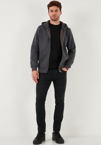 Sivi dukserica sa patentnim zatvaračem i kontrastnim unutarnjim podstavljanjem, nosi se preko crne majice, uz crne traperice i crne tenisice. Jednostavna tekstura.