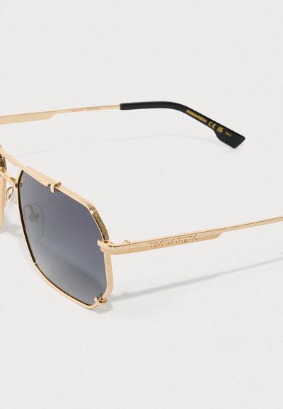 Gafas de sol de metal dorado con lentes oscuros hexagonales, con acentos grabados y patillas rectas y elegantes. Detalles en negro en las puntas.