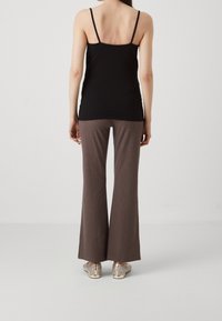 Top noir ajusté, pantalon évasé marron avec un motif subtil, et chaussures métalliques avec des découpes. Vue de dos affichée.