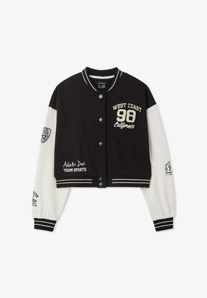 Giacca varsity in bianco e nero con design cropped, caratterizzata da testo ricamato, bottoni a pressione e polsini a righe. Decorata con vari patch.