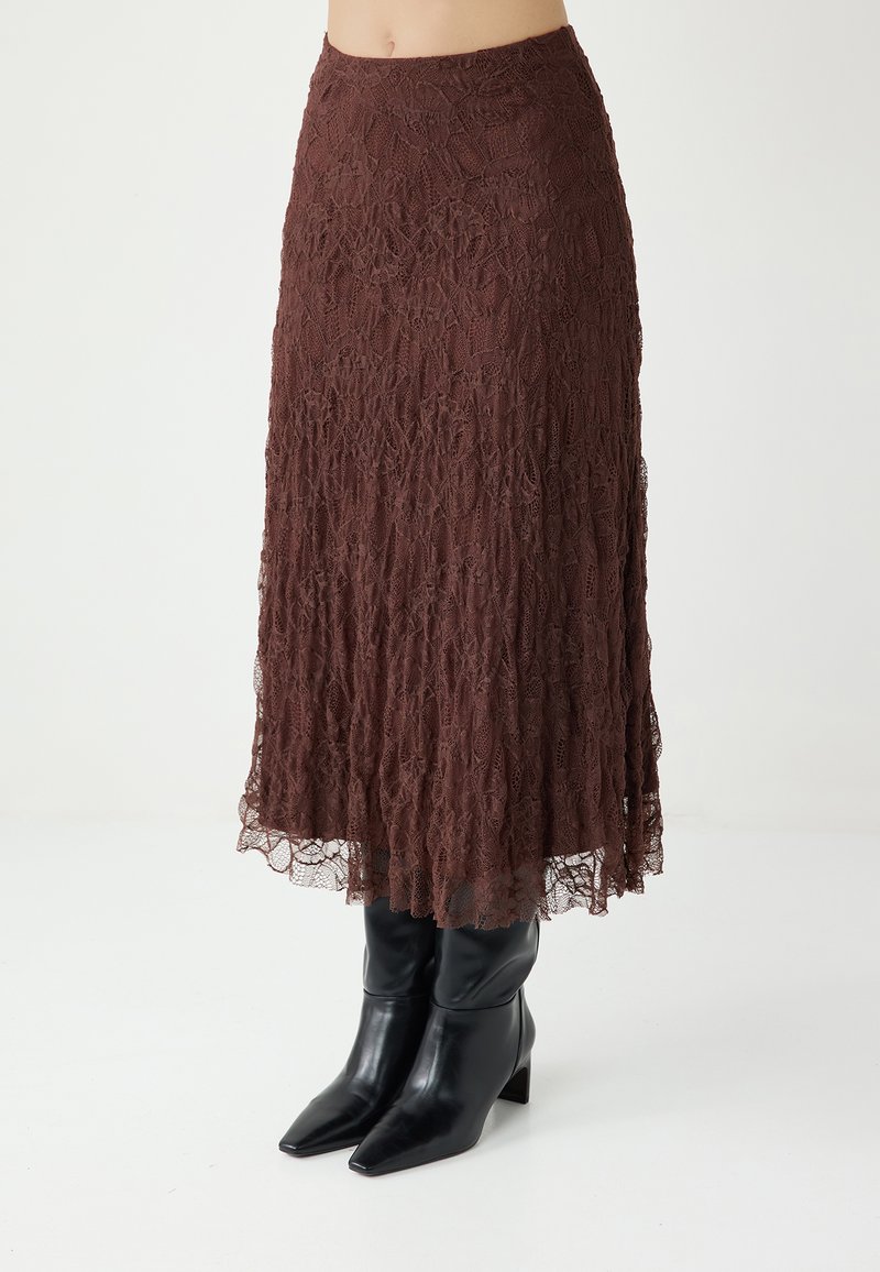 Jupe midi en dentelle marron avec une silhouette fluide, présentant un motif texturé et une taille ajustée, associée à des bottes noires élégantes à bout pointu.