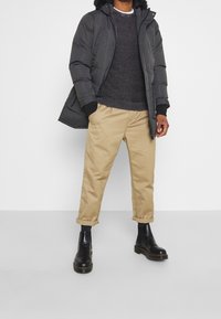 Czarna pikowana kurtka z kapturem, szary sweter dziany, beżowe spodnie z mankietami i czarne botki za kostkę z masywną podeszwą.