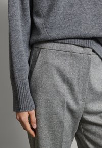 Suéter gris de punto acanalado con mangas largas, combinado con pantalones a medida de un gris claro. La tela tiene una textura suave con un patrón sutil.