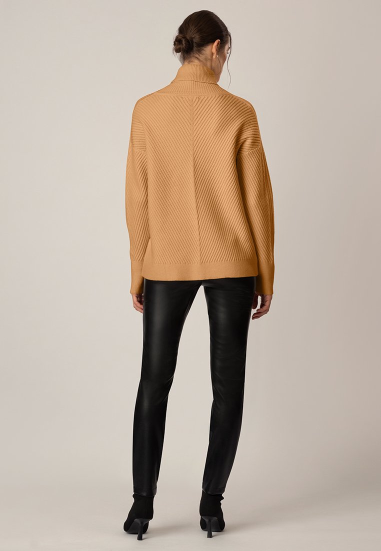 Beige gerippter Rollkragensweater mit lockerem Schnitt, kombiniert mit engen schwarzen Lederhosen und hohen Stiefeletten.