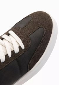 Mörkbrun sneaker med slät läder och texturerad mocka, vita snören och en kontrasterande gummisula. Rundad tådesign.