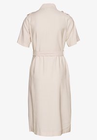 Béžové šaty s krátkými rukávy, límečkem, páskem v pase a zdobením na ramenou. Hladká látka, délka ke kolenům, minimalistický design.