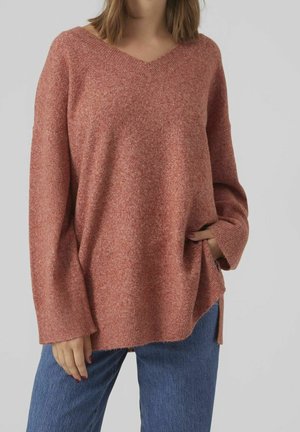 Pullover oversize con scollo a V in un morbido e testurizzato maglione rosa-rossiccio. Presenta spalle abbassate e aperture laterali, abbinato a jeans in denim blu.