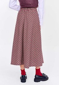 Karovaná midi sukňa v červenej, čiernej a krémovej farbe. Elastický pás s voľným strihom. Skombinovaná s čiernymi topánkami a rebrovanými červenými ponožkami.