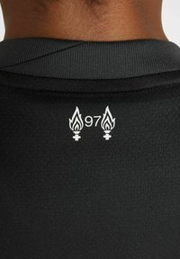 Svart träningströja med en texturerad tyg; har vita grafiska detaljer av lågor och "97" på baksidan nära kragen.